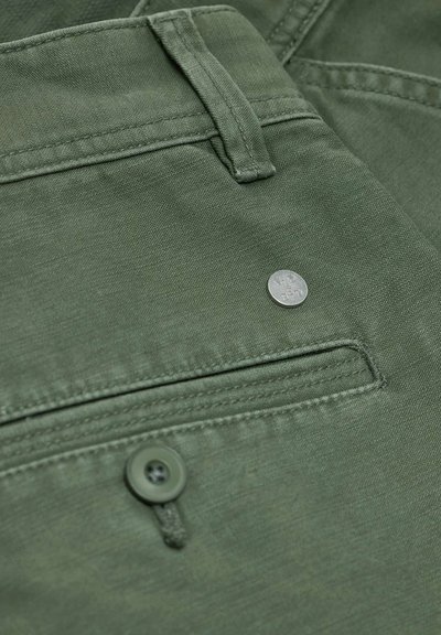 Pantaloni di cotone verdi con tasca frontale dotata di un bottone in metallo e dettagli cuciti, che enfatizzano una texture liscia e un design casual.