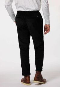 Zwarte corduroy broek met een tapered fit, elastische tailleband en achterzakken, gecombineerd met bruine leren boots en opgerolde mouwen.