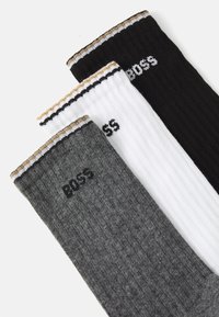 Three pairs of ribbed socks in black, white, and dark gray, each featuring a contrasting striped cuff and "BOSS" logo.