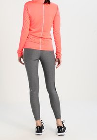 Långärmad ljusrosa topp med en vertikal söm. Grå tighta leggings med svart sidpanel. Svarta sportskor med vita accenter.