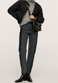 Veste matelassée noire portée sur un pull gris, associée à un jean foncé avec des panneaux latéraux. Bottines noires et sac noir avec des ferrures dorées.