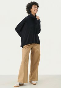 Donker marineblauw oversized coltrui met een relaxed fit, gecombineerd met beige wijde broek en witte sneakers met zwarte strepen.