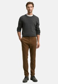 Pull gris avec un col blanc, pantalon marron et bottes noires. Le pull a des poignets côtelés ; le pantalon est droit et à texture lisse.
