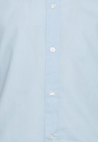 Světle modrá zapínací košile vyrobená z bavlny; má rovný střih, přední légu s bílými knoflíky a žádné vzory nebo další ozdoby.