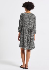 Schwarz-weißer, gemusterter Kleid mit Dreiviertelärmeln, gerafftem Bund und ausgestellt geschnittenem Rock. Glattes Gewebe mit geometrischen Formen.