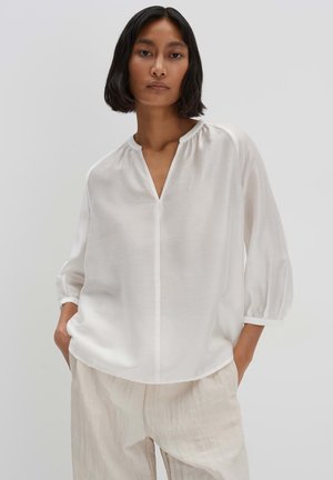Blusa bianca con scollatura a V, maniche lunghe a sbuffo e leggere arricciature sul collo, realizzata in tessuto leggero e testurizzato.