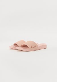 Rosa sko med glatt, matt finish. Har en bred stropp og strukturert fotseng, merket med "REEF" i kontrastfarge.