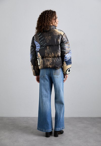 Giacca nera imbottita con motivi astratti multicolori, abbinata a jeans a gamba larga blu chiaro e stivali neri con tacco blocco.