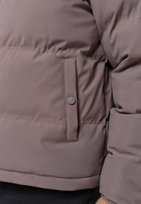 Puchowa kurtka w stonowanym mauve o gładkiej teksturze. Posiada kieszeń z zatrzaskiem po boku. Dopasowane mankiety i dół z elastanem.