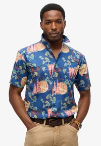 Korte mouwen blouse in blauwe stof met kleurrijke bloemen- en architectonische patronen, voorzien van een kraag en een borstzakdetail.