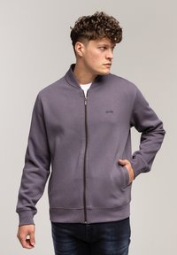 Szara bluza zapinana na zamek, wykonana z miękkiego materiału, z stójką, z małym logo na klatce piersiowej i bocznymi kieszeniami.