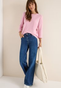 Lyserød, bluse med lange ærmer; blå, vide jeans; hvid, struktureret skuldertaske med dobbelte håndtag; glat tekstur; afslappet pasform.