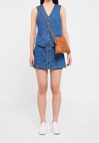 Jeansväst med knappar och V-ringning, i kombination med en jeanskorts med framknäppning. Vävd brun axelremsväska. Vita sneakers.