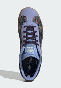 Floral-patterned sneaker featuring a blue suede upper, navy accents, and a beige rubber sole. Includes a flat lace system and branding on the tongue.
