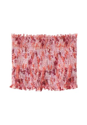 Femme aux longs cheveux foncés porte un top rose sans bretelles, un short blanc, des sandales argentées, et porte un petit sac tissé sur un fond uni.