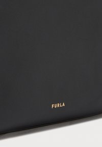 Sac en cuir texturé noir avec une finition lisse. Présente un logo "FURLA" doré en bas. Design simple, forme rectangulaire.