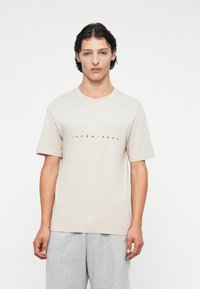 Beige bomulds t-shirt med korte ærmer og rund hals, med "JACK & JONES" trykt i sort på brystet.