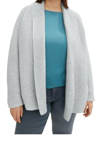 Cardigan lavorato a maglia grigio chiaro con apertura frontale, texture a coste e maniche lunghe, indossato sopra un top verde teal e abbinato a jeans scuri.