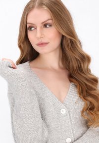 Hellgraue Strickjacke mit tiefem V-Ausschnitt, gerippten Bündchen und drei weißen Knöpfen, mit einer weichen, strukturierten Oberfläche.