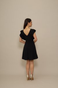 Black dress with short ruffled sleeves and a deep V-back, featuring a fitted bodice and flared skirt, paired with metallic high-heeled shoes.