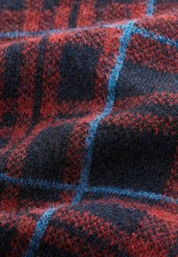 Wollstoff mit rotem und dunkelblauem Karomuster, das dünne hellblaue Linien aufweist, in einer Nahaufnahme gezeigt, mit sichtbarer Textur und Fasern.