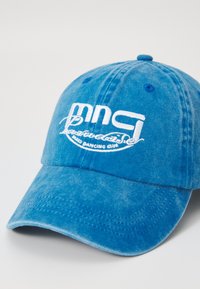 Casquette de baseball en coton bleu avec texte brodé blanc et visière courbée. Le matériau a une finition texturée avec des variations subtiles.