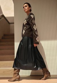 Brown argyle sweater over a black leather skirt and light brown heeled boots. Smooth textures with contrasting patterns and colors.