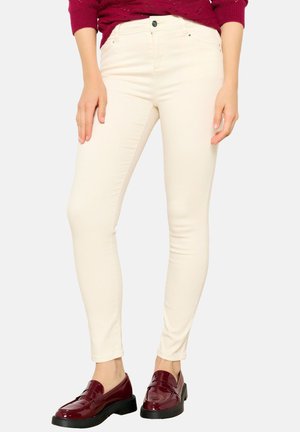 Beige skinny jeans with a smooth texture, five-pocket design, and a front button closure, paired with burgundy patent loafers.