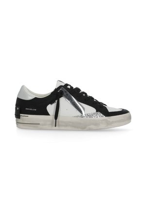 Sneaker basse nero e bianco con lacci neri, dettaglio glitter argento sul bordo della suola e una targhetta argento attaccata vicino ai lacci.