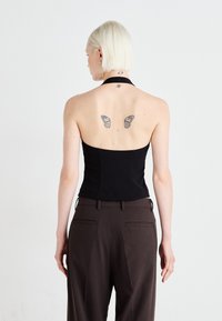 Black strapless top with a fitted design. Paired with brown high-waisted trousers. Notable butterfly tattoos on the back.