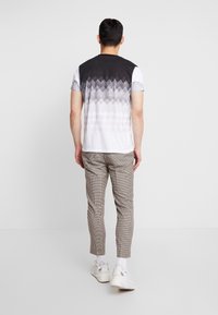 Pánská košile v černo-bílé barvě s přechodovým vzorem diamantů. Doplněná o šedé kostkované kalhoty a bílé tenisky.