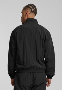 Svart lättviktig jacka med hög krage, elastiska manschetter och midjeband. Enkelt design, texturerat tyg och inga synliga mönster eller hårdvara.