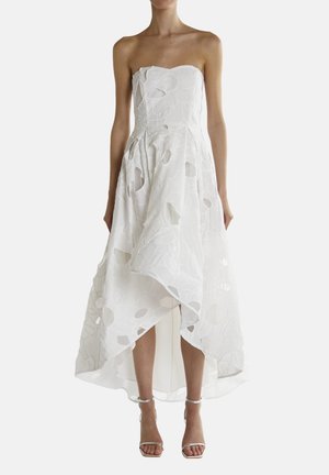 Vestido blanco sin tirantes que presenta una tela en capas con cortes circulares, un dobladillo asimétrico y un acabado suave y texturizado.