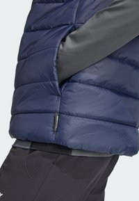 Marineblå isoleret puffer vest med horisontalt quiltet design, der har en sidelomme og grå stofdetalje på skuldrene for ekstra komfort.