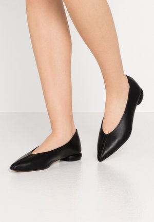 Black leather flats with a pointed toe design, featuring a low, rounded heel and visible stitching detail along the front edge.