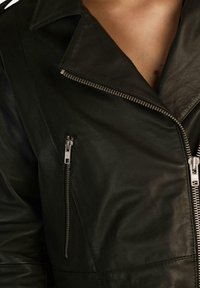 Giacca di pelle nera con collo a punte, zip in argento e due tasche con zip sul davanti. La texture è liscia e lucida.