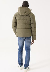 Chaqueta acolchada en verde oliva con un diseño de rombos, capucha con cremallera y puños elásticos, combinada con jeans azules y zapatillas blancas-verdes.