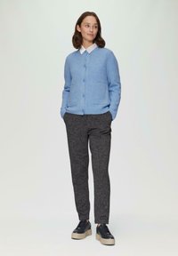 Himmelblauer, gerippter Strickcardigan mit Knopfverschluss und zwei vorderen Taschen, kombiniert mit dunklen, strukturierten Hosen und klobigen schwarzen Sneakers.