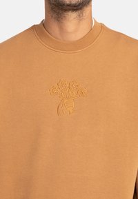 Sudadera marr�ón de tejido suave con un diseño floral bordado tonal en el pecho. El cuello redondo y los puños acanalados completan el look.