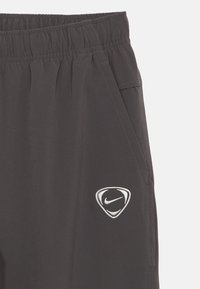 Σκούρο γκρι αθλητικό παντελόνι με ελαστική μέση, πλαϊνές τσέπες και εμφανές λευκό λογότυπο Nike κοντά στο τελείωμα. Λεπτό, ελαφρύ ύφασμα.