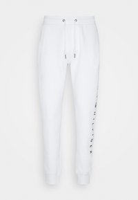 Vita sweatpants med elastisk midja, dragsko, mer än vristen och svart vertikal "Tommy Hilfiger" text på höger ben.