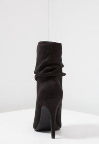 Botte noire à la cheville avec un design flou, fabriquée en suède, dotée d'un talon aiguille haut et d'une texture lisse.