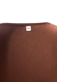 Camicia marrone a maniche corte realizzata in tessuto morbido. Presenta un colletto rotondo e un piccolo etichetta cucita sul retro con il nome del marchio.
