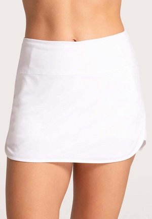 Waist to mid-thigh view of a person wearing a plain white athletic skort with a curved hem against a neutral background.
