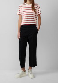 T-shirt blanc coupé avec des rayures horizontales rouges, associé à un pantalon noir coupé et des baskets blanches avec des semelles texturées.