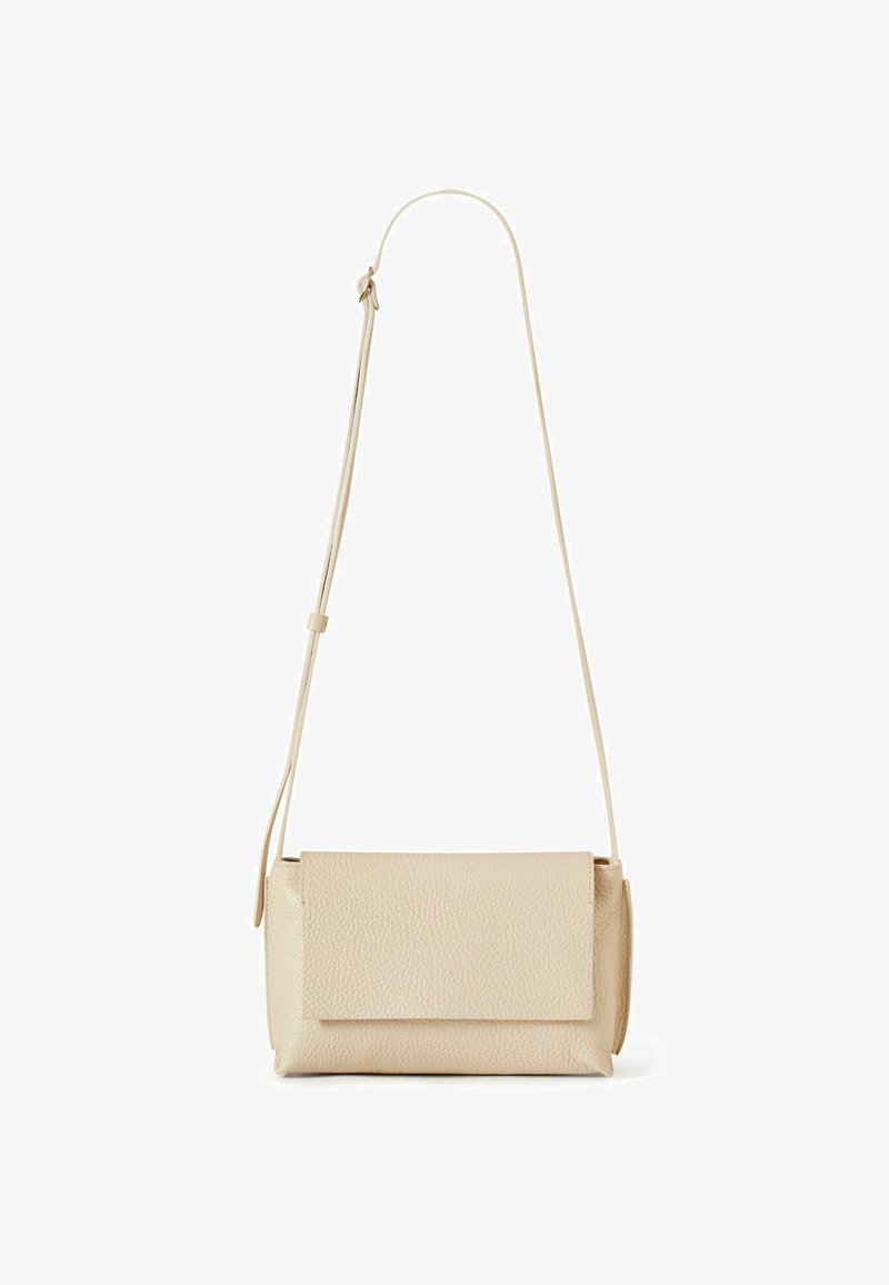 Béžová texturovaná kožená kabelka přes rameno s klopou a nastavitelným tenkým ramenním popruhem na bílém pozadí.