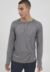 Langærmet grå henley skjorte med tekstureret stof, der har en rund halsudskæring og tre knapper foran. Rundet kantdetalje.