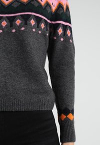 Šedý pletený svetr s barevnými geometrickými vzory v růžové, oranžové a zelené kolem výstřihu a manžet. Měkká textura, přiléhavý design.