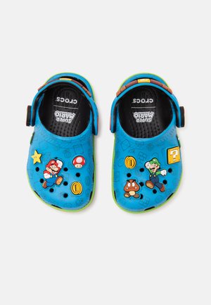 Niebieskie dziecięce Crocsy z postaciami i ikonami Super Mario, z regulowanymi paskami na pięcie i zielonymi podeszwami.
