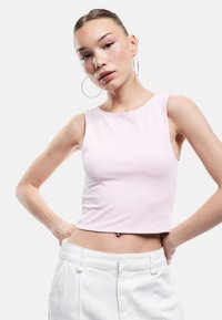 Lichtroze cropped tanktop van gladde stof met een ronde halslijn en brede schouderbanden, gecombineerd met hoge witte broeken.